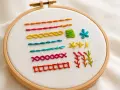 Embroidery hoop with various colorful stitches and patterns on white fabric.