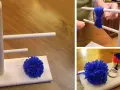 Creazione di pon pon di lana fai da te con un attrezzo in legno. Un pompon blu è pronto, un altro è in lavorazione.
