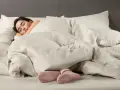 Donna dorme avvolta in lenzuola in microfibra che sembrano farla sudare, con solo i piedi in calzini rosa visibili.