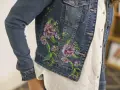 Giacca di jeans con un bellissimo ricamo su stoffa di fiori colorati e foglie verdi.