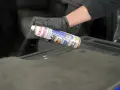 Mano con guanto nero spruzza spray Idrostop su tessuto grigio per impermeabilizzare.