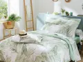 Un letto preparato per l'estate con biancheria a tema tropicale, un cappello di paglia e una borsa di vimini.