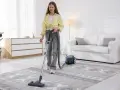 Ragazza aspira un tappeto con un aspirapolvere. Il tappeto ha un disegno geometrico e sembra avere una base in gomma sotto.