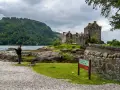 Uomo con cornamusa indossa un kilt scozzese davanti a un castello.