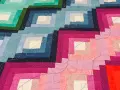 Dettaglio di una coperta realizzata con la tecnica patchwork, con blocchi a gradiente di colore dal blu al rosa, rifinita con cuciture decorative.