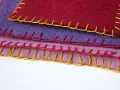 Tessuti colorati sovrapposti, rifiniti con un punto coperta giallo, rosa e rosso.