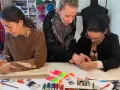 Tre donne si dedicano al cucito a mano, circondate da fili colorati, forbici e cartamodelli.