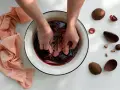 Mani che tingono tessuti con il tè in una bacinella. Pezzi di avocado e tessuti color pesca completano la scena.