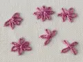 Close-up of five small, pink embroidered daisy stitches on a cream fabric background.