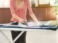 Donna stira un paio di jeans su un asse da stiro, usando un ferro da stiro a vapore. Impara come stendere i pantaloni per un look impeccabile.