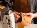 Mani esperte che cuciono la pelle con filo e ago, creando un dettaglio decorativo su un pezzo di cuoio.