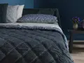 Letto con copriletto trapuntato blu scuro, cuscini floreali e un dettaglio che ricorda che il velluto si rovina con acqua.