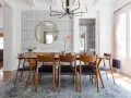 Tavolo da pranzo in legno con sedie in pelle nera, tappeto sotto il tavolo da pranzo si, con carta da parati a motivi geometrici e specchio rotondo.