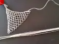Un ago con filo bianco e un pezzo di rete a maglie, un tipo di ricamo eseguito su una rete a maglie, con un nastro rosso in alto.