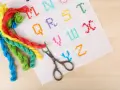 Fili colorati e forbicine pronti per ricamare nomi punto catenella su tela bianca con lettere dell'alfabeto.