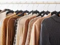 Una fila di capi d'abbigliamento in tonalità neutre, tra cui un maglione lavorato a maglia e un blazer in tessuto cupro lavaggio, pronti per essere indossati.