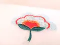 Un fiore stilizzato con petali azzurri e paillettes, un cuore rosso al centro e perline arancioni. Un'opera di ricamo francese che cattura la luce.