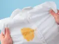 Come togliere le macchie gialle dalla biancheria colorata: una camicia bianca macchiata di giallo, tenuta in mano.