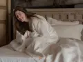 Ragazza sorridente avvolta in lenzuola di lino bianco su un letto. Perfetto per le misure lenzuola una piazza e mezza.