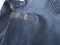 Dettaglio di un tessuto di jeans blu con un'area rattoppata con filo bianco, che mostra la cura nel rattoppare jeans.