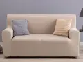 Divano con copridivano in tessuto color crema, due cuscini decorativi a maglia, uno grigio e uno beige.