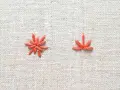 Two orange embroidery stitches on a textured linen fabric.