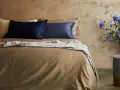 Letto con lenzuola color tabacco, cuscini blu e beige, coperta grigia. Il miglior tessuto per lenzuola per un sonno di qualità.