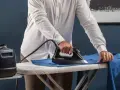 Uomo con camicia bianca che stira i panni su un asse da stiro, con un ferro a vapore e una caldaia Rowenta.