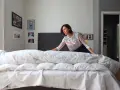 Donna con maglia a righe prova a mettere il copripiumino su un letto disfatto.