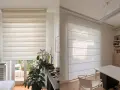 Due diversi tipi di tende: una a rullo a strisce alternate e una a pacchetto in tessuto leggero, che filtrano la luce in ambienti moderni.