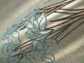 Dettaglio di un tessuto con ricamo floreale in punto pieno, con fili blu e marroni su sfondo cangiante.