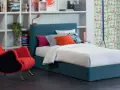 Letto una piazza e mezza con testiera blu, cuscini colorati e una poltrona rossa vivace.