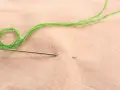 Ago e filo verde pronti per ricamare nome a mano su stoffa color pesca.