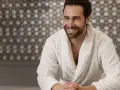 Uomo sorridente in un morbido accappatoio che asciuga bene, con uno sfondo a mosaico.