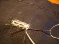 Ago e filo bianco creano un punto occhiello a mano su tessuto scuro.