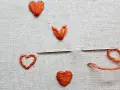 Un ago con filo arancione pronto per creare un altro cuore ricamato a mano su tela grezza.