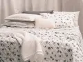 Un letto accogliente con biancheria a fiori e righe, coperte morbide e cuscini che invitano al riposo, come in un sogno di letti all'americana.