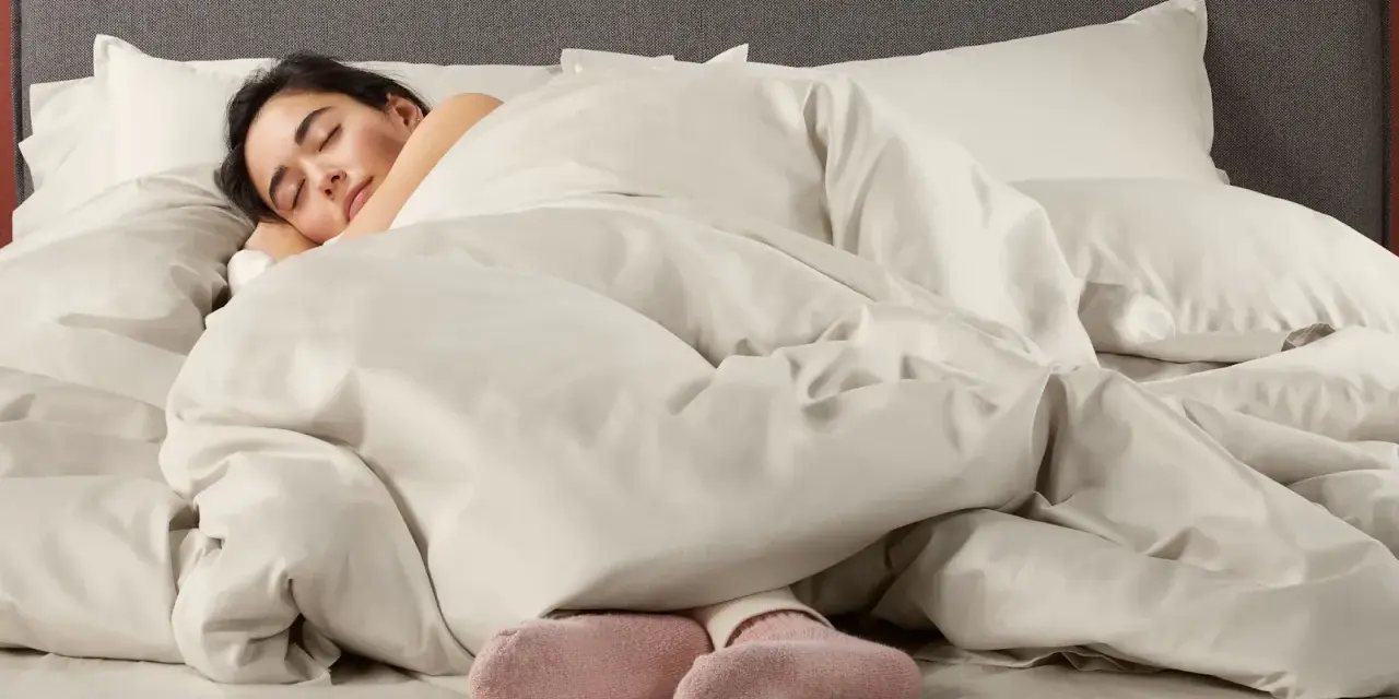 Donna dorme avvolta in lenzuola in microfibra che sembrano farla sudare, con solo i piedi in calzini rosa visibili.