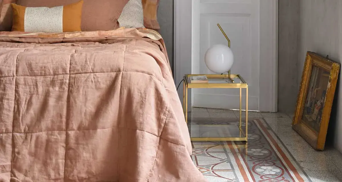 Un morbido quilt matrimoniale color pesca, con cuciture a quadri, adorna un letto in una stanza elegante.