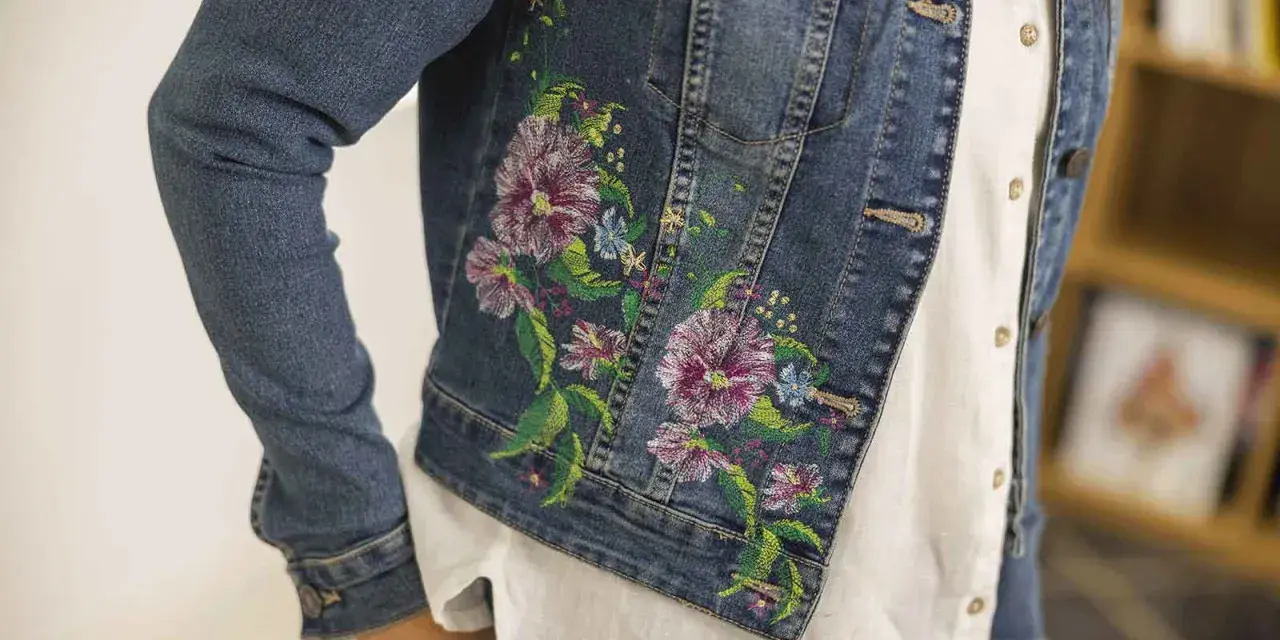 Giacca di jeans con un bellissimo ricamo su stoffa di fiori colorati e foglie verdi.
