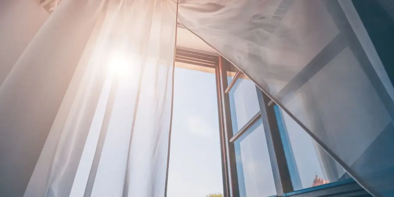 Tende leggere e ariose, fissate senza fare buchi, fluttuano dolcemente con la brezza che entra da una finestra aperta, illuminata dal sole.