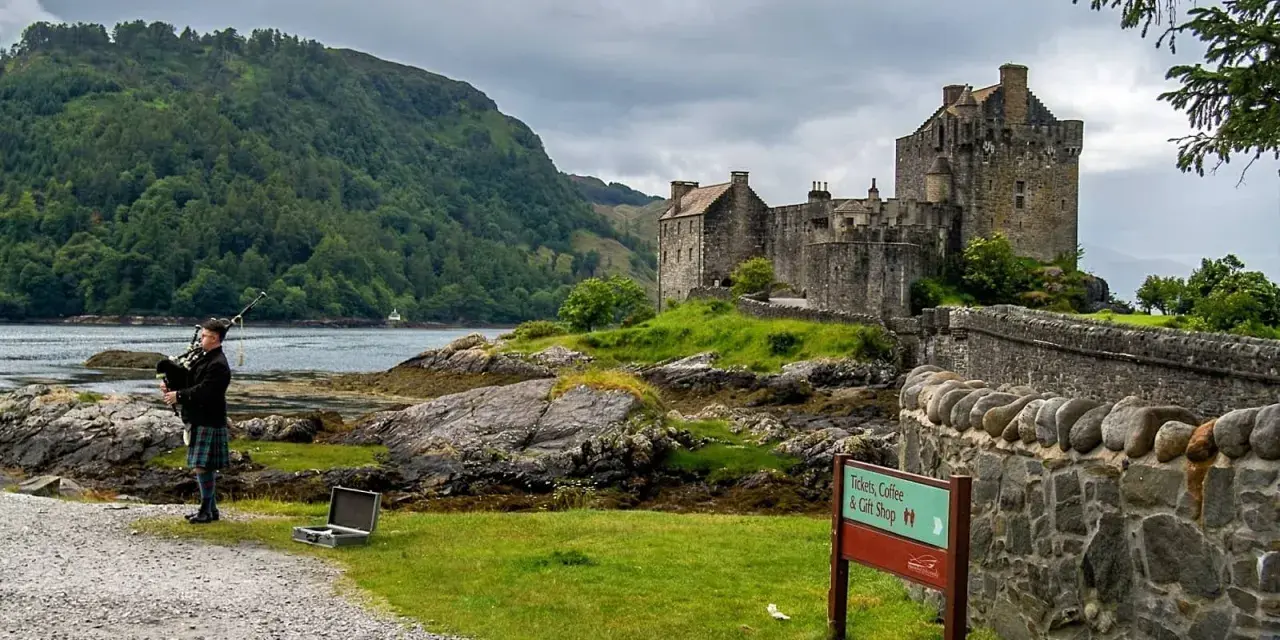Uomo con cornamusa indossa un kilt scozzese davanti a un castello.