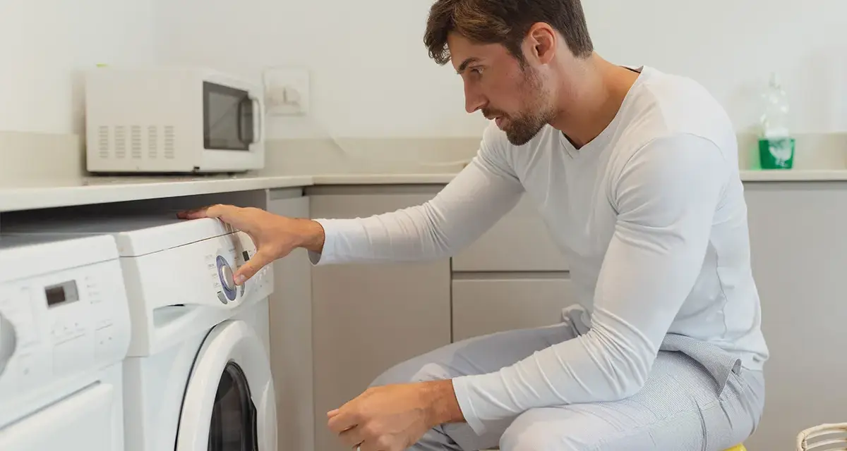 Uomo in pigiama imposta la lavatrice per asciugare la ciniglia.