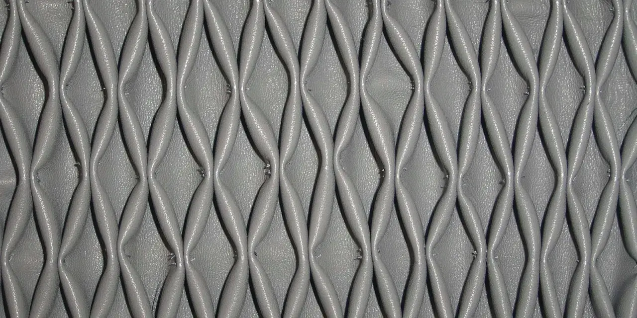 Ricamo in pelle grigia con un motivo a nido d'ape, che crea un effetto tridimensionale e geometrico.