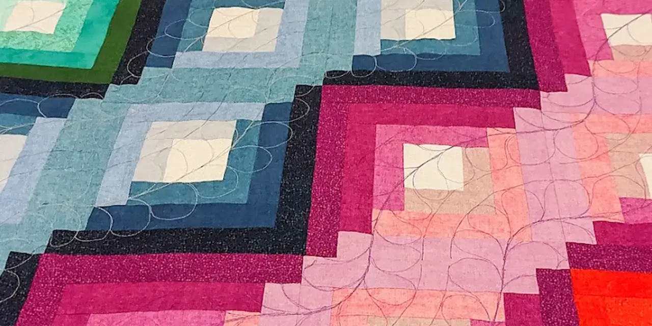 Dettaglio di una coperta realizzata con la tecnica patchwork, con blocchi a gradiente di colore dal blu al rosa, rifinita con cuciture decorative.