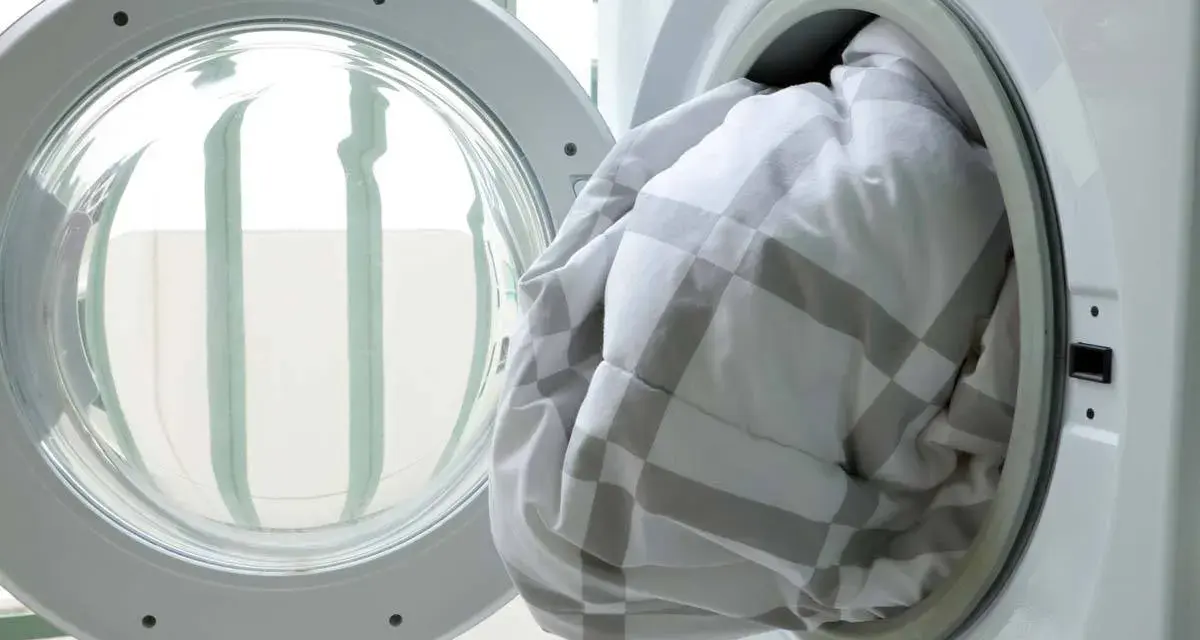 A white and grey checkered duvet being loaded into a washing machine.