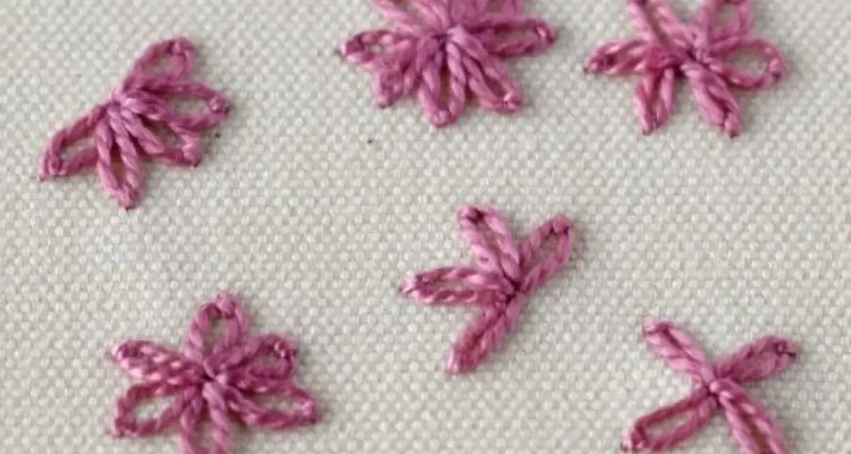 Close-up of five small, pink embroidered daisy stitches on a cream fabric background.