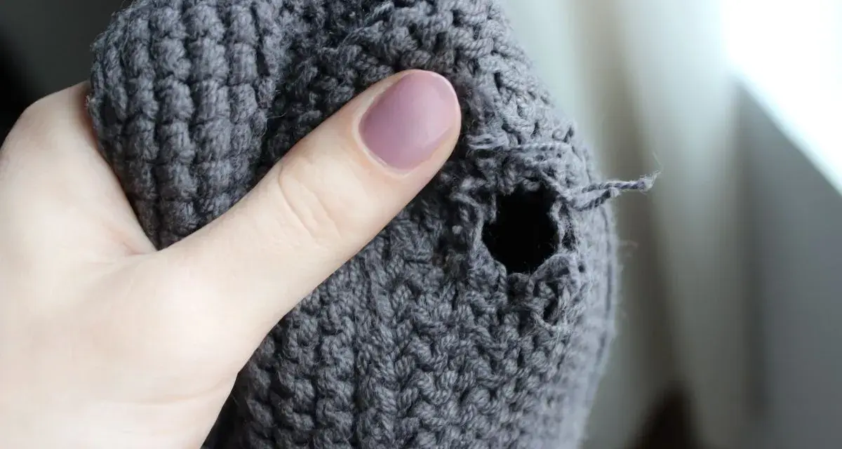 Dito un buco in un maglione grigio, pronto per imparare come rammendare uno strappo a mano.