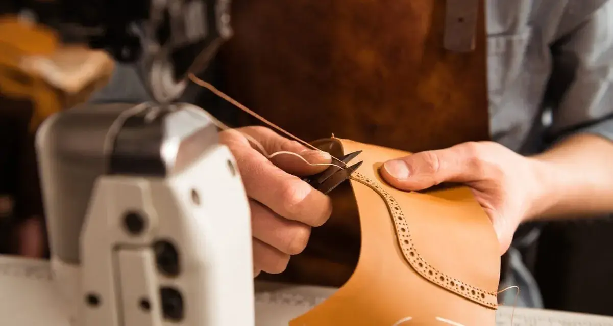 Mani esperte che cuciono la pelle con filo e ago, creando un dettaglio decorativo su un pezzo di cuoio.