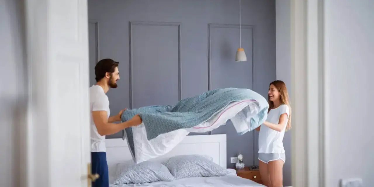 Coppia felice che cambia le lenzuola, un gesto che ci ricorda ogni quanto cambiare le lenzuola per un sonno più sano.